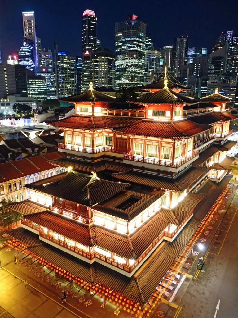 Aerial view of the Buddha Tooth Relic Temple in Singapore, beautifully lit against a modern cityscape.